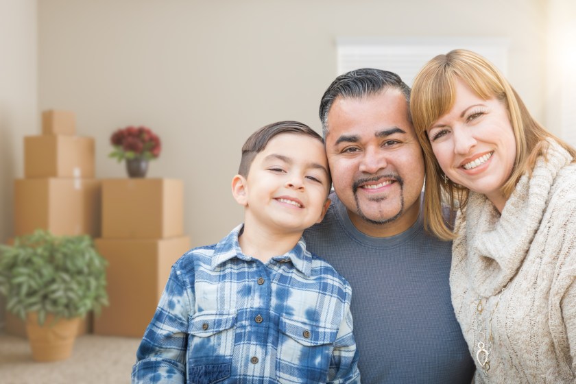 Mixed Race Family In Empty Room With Moving Boxes and Plants.