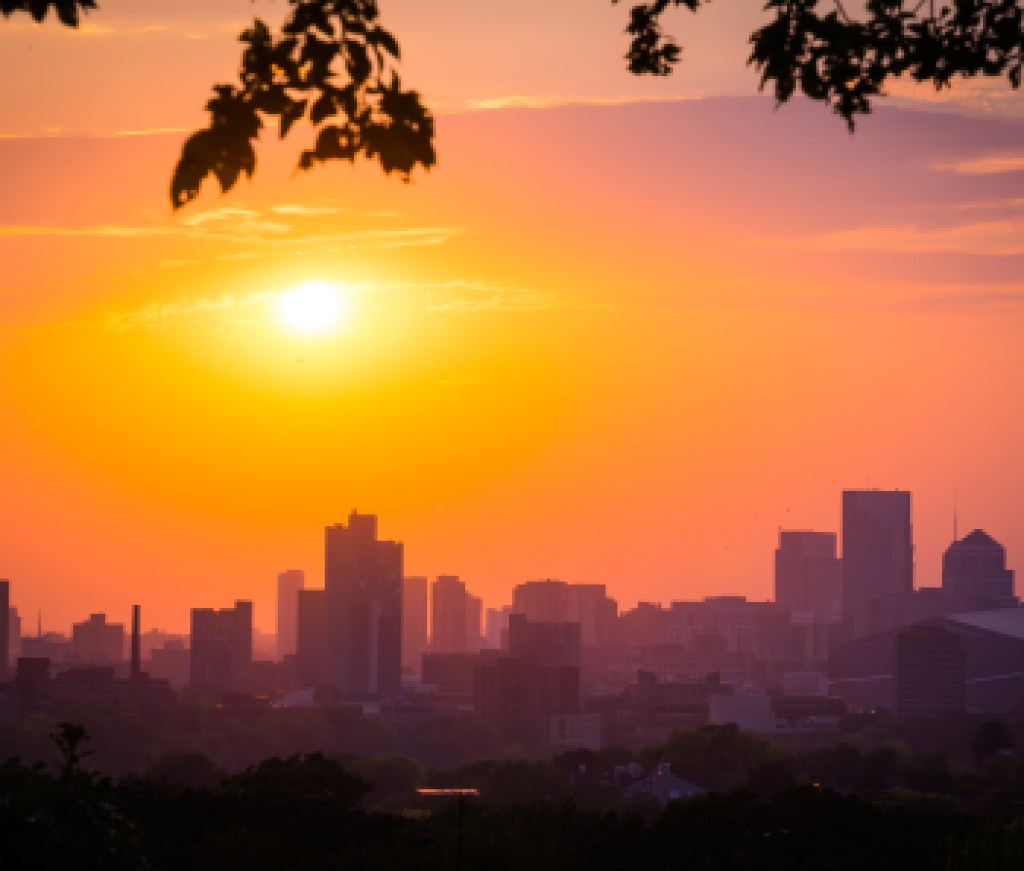 sunset with the minneapolis minnesota skyline framed with leaves and branches. sky is pink, orange, blue and purple.