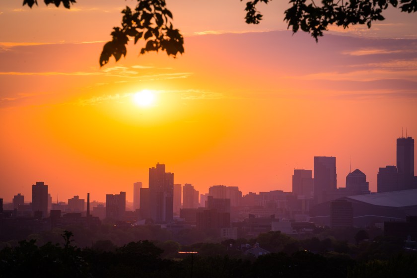 sunset with the minneapolis minnesota skyline framed with leaves and branches. sky is pink, orange, blue and purple.