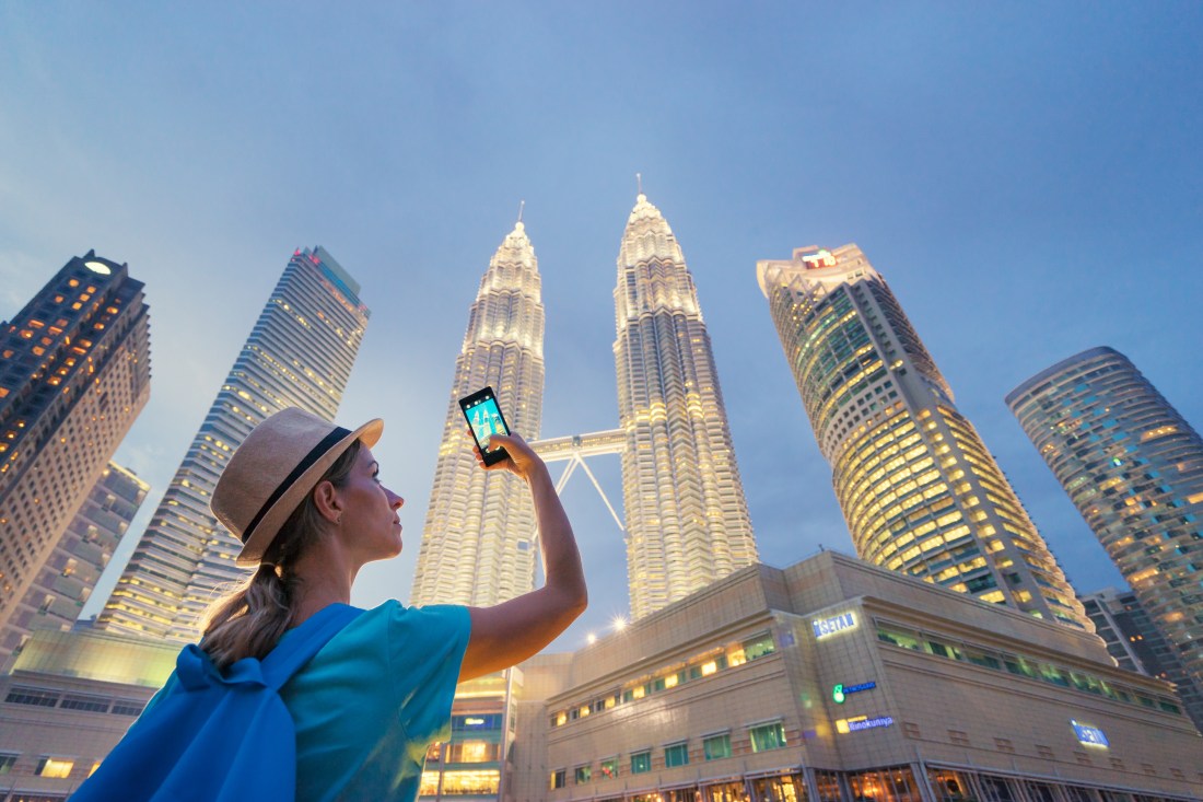 Travel and technology. Young  woman taking photo with her smartphone of Petronas Twins Towers in Kuala-Lumpur at evening, Malaysia, 23 November 2015.