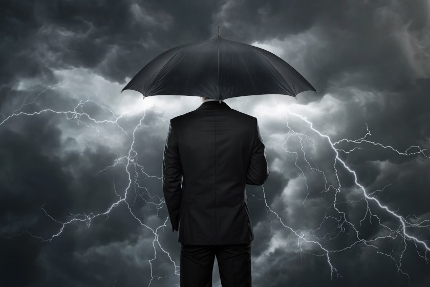 Businessman with umbrella standing in front of storm