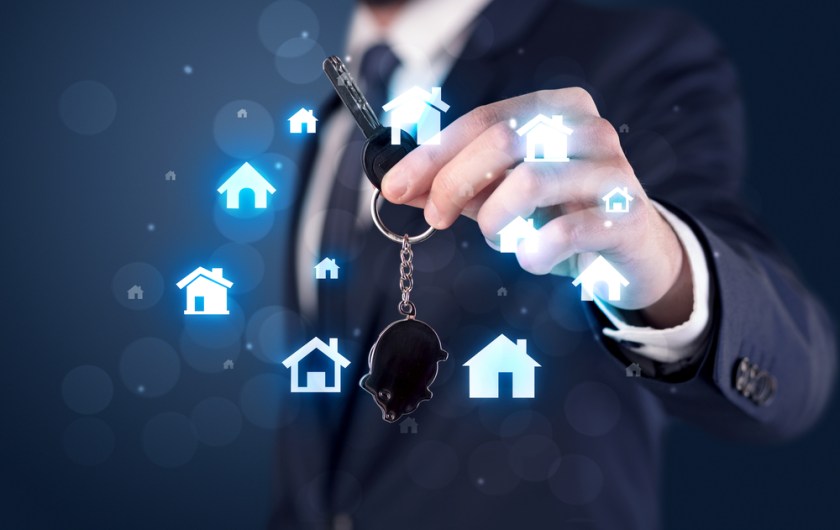 Businessman-in-suit-holding-keys-with-house-graphics-around-and-dark-background-1