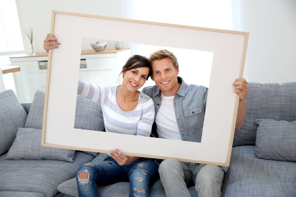 Cheerful-young-couple-holding-picture-frame-to-look-through