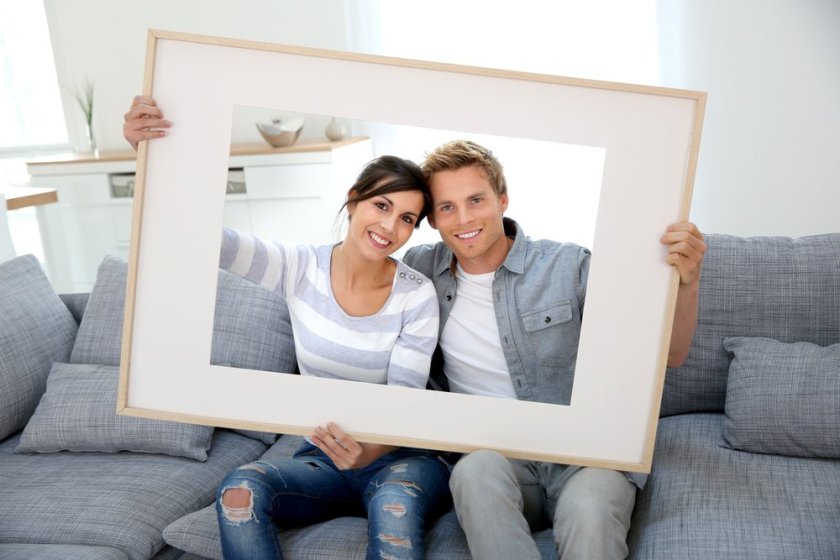 Cheerful-young-couple-holding-picture-frame-to-look-through