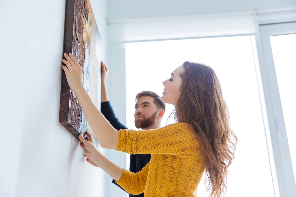 Happy-couple-hanging-picture-on-the-wall-at-home