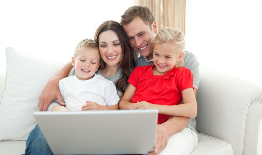 Joyful-family-using-a-computer-sitting-on-sofa-in-the-living-room