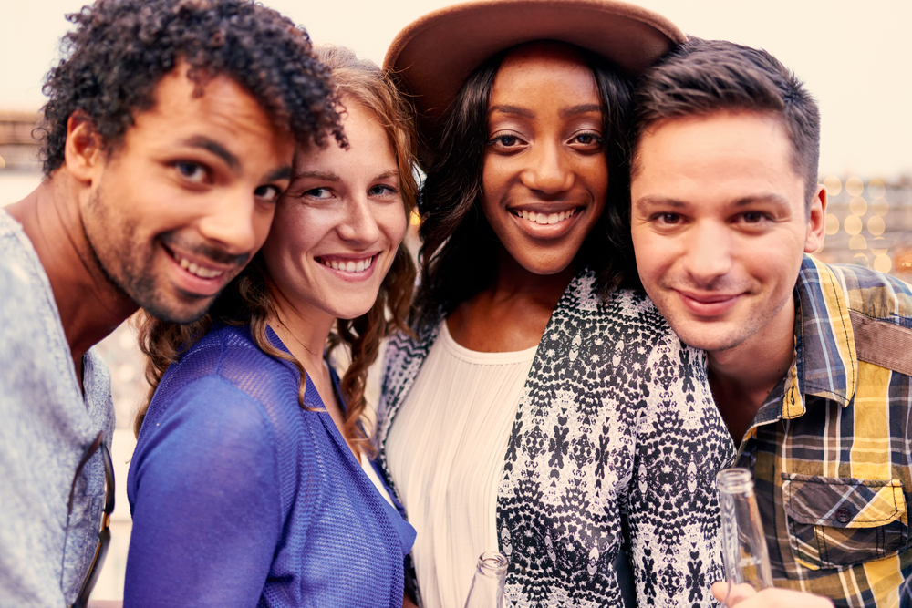 Multi-ethnic-millenial-group-of-friends-taking-a-selfie-photo-with-mobile-phone-on-rooftop-terrasse-at-sunset