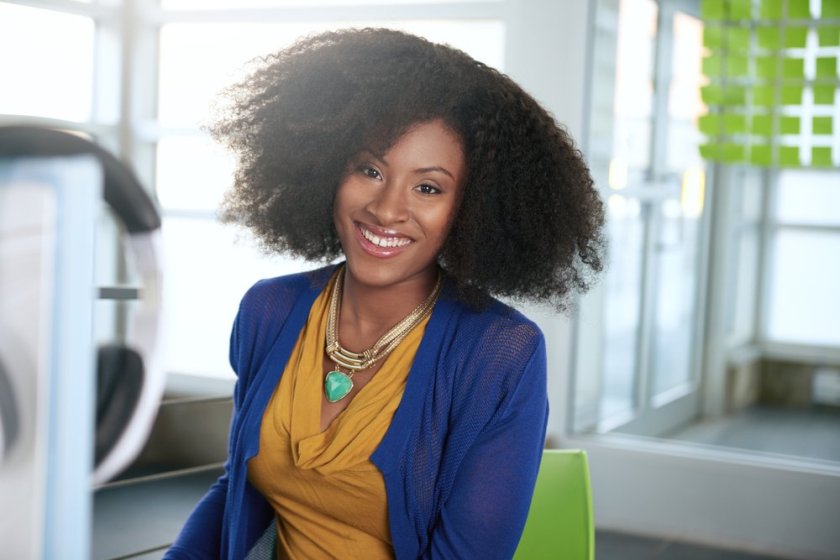Portrait-of-a-smiling-woman-with-an-afro-at-the-computer-in-bright-glass-office