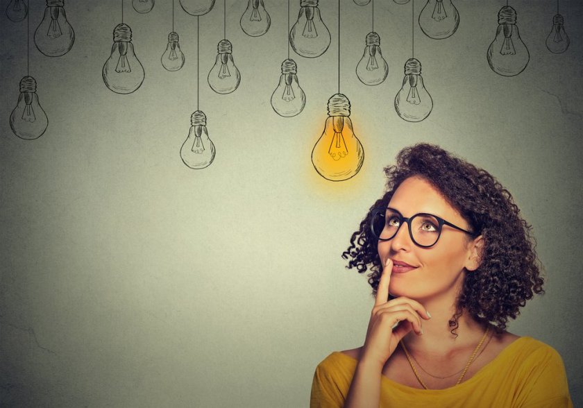 Thinking-woman-in-glasses-looking-up-with-light-idea-bulb-above-head-isolated-on-gray-wall-background-1