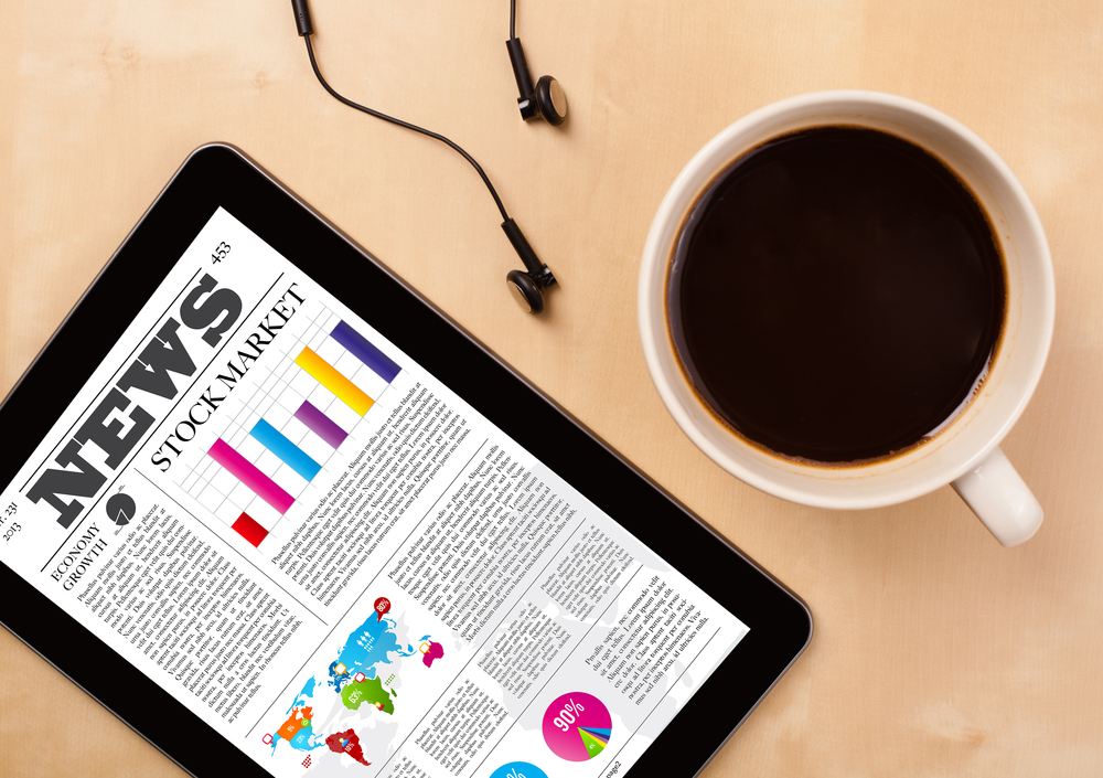 Workplace-with-tablet-pc-showing-latest-news-and-a-cup-of-coffee-on-a-wooden-work-table-close-up