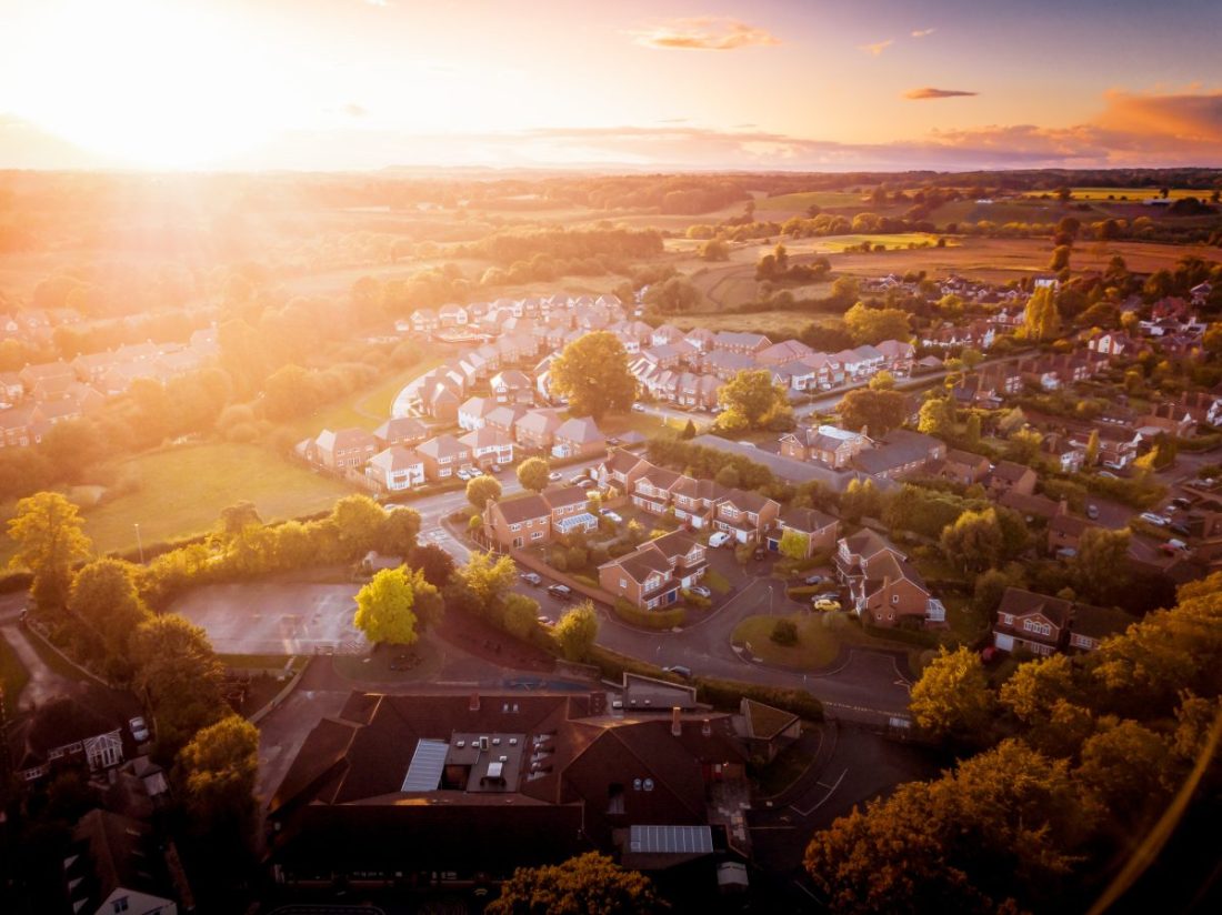 Sun rising above a traditional British housing estate with countryside in the background.