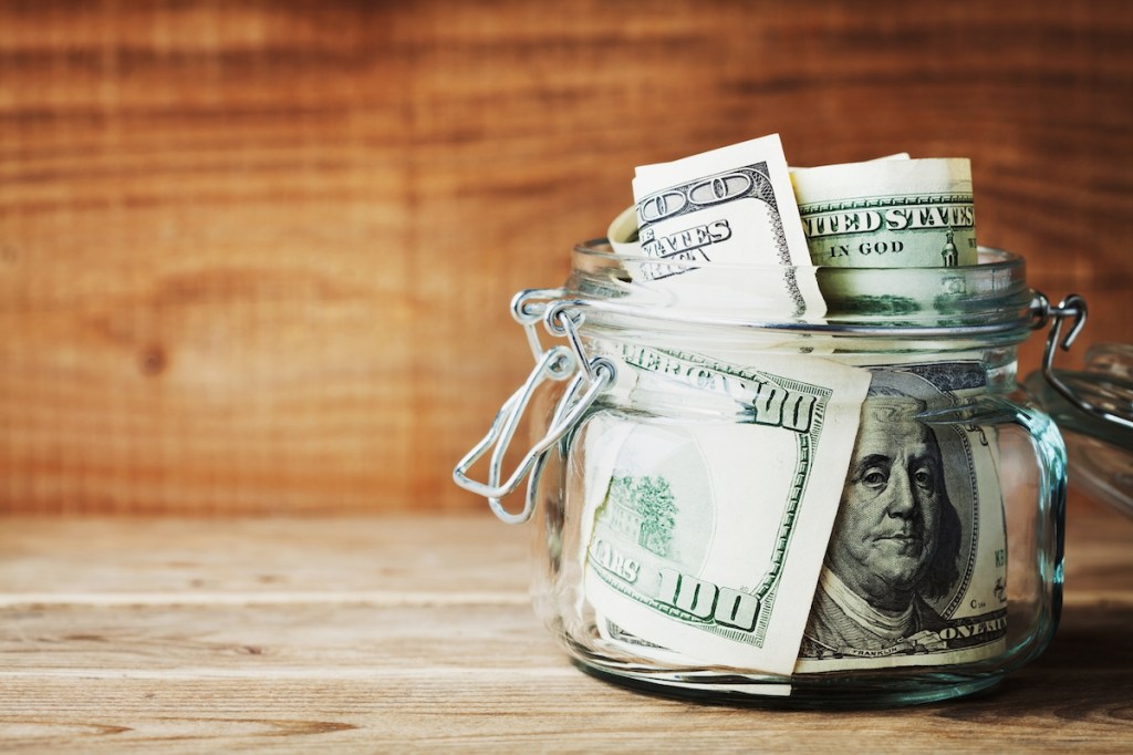 Dollar bills in glass jar on wooden background. Saving money concept.