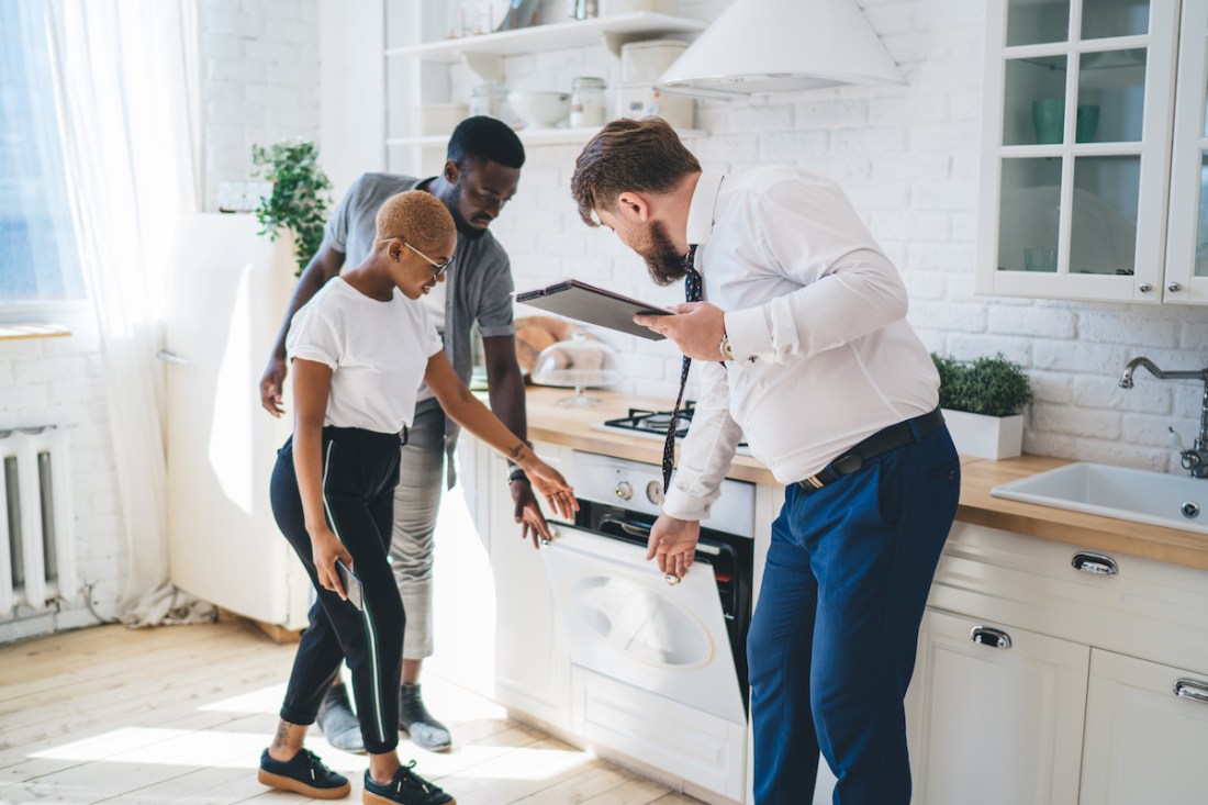 Confident estate agent showing kitchen to African American thoughtful couple