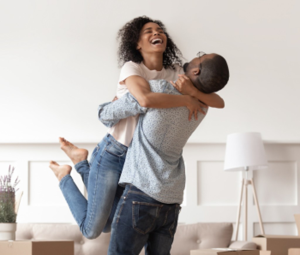 Husband lifting happy wife celebrating moving day with boxes