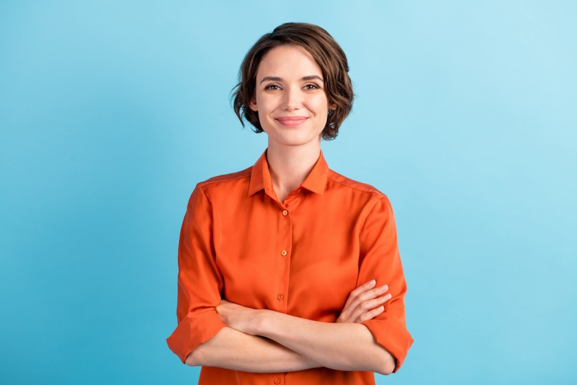 Photo of attractive charming lady cute bobbed hairdo arms crossed self-confident person worker friendly smile good mood wear orange office shirt isolated blue color background