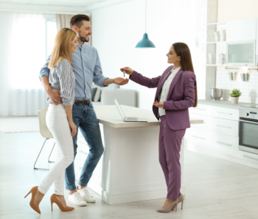Female real estate agent giving house key to couple indoors